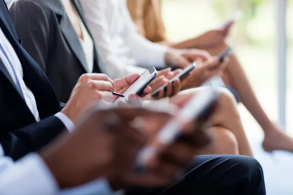 Varios candidatos sentados usando sus teléfonos móviles y tabletas durante la etapa de selección de reclutamiento de personal.